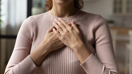 Close up cropped young woman holding folded hands on heart chest, feeling grateful. Sincere kind...