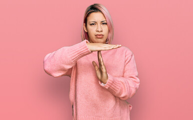 Hispanic woman with pink hair wearing casual winter sweater doing time out gesture with hands,...