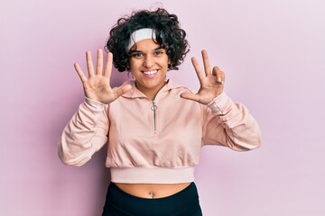 Young hispanic woman with curly hair wearing sportswear showing and pointing up with fingers number eight while smiling confident and happy.