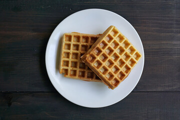 Warm waffles in a white plate on a black wooden table                 