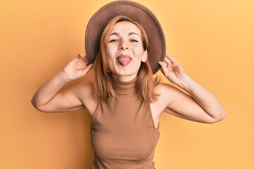 Young caucasian woman wearing hat sticking tongue out happy with funny expression.