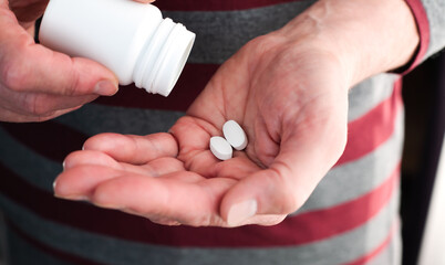 The senior man hands are pouring white pills from a bottle. Caring for the health of the elderly. Medical concept. Close-up.