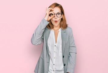 Young caucasian woman wearing business style and glasses doing ok gesture shocked with surprised face, eye looking through fingers. unbelieving expression.