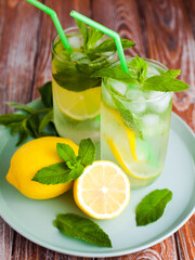 Two glass with natural refreshing lemonade or mojito cocktail with lemon, mint and ice cubes. Cold summer beverage on wooden background. Close-up.