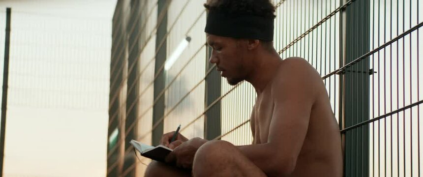 Young African American male writing lyrics for his song on a basketball court. Aspiring rap artist dreaming of becoming future star. Shot with 2x anamorphic lens