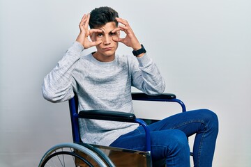 Young hispanic man sitting on wheelchair trying to open eyes with fingers, sleepy and tired for morning fatigue