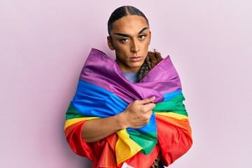 Hispanic man wearing make up and long hair wrapped in rainbow lgbtq flag skeptic and nervous, frowning upset because of problem. negative person.