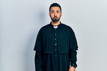 Handsome hispanic man with beard wearing catholic priest robe depressed and worry for distress, crying angry and afraid. sad expression.