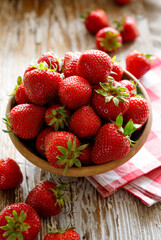 Fresh strawberries in a ceramic bowl on a wooden table, close up vie