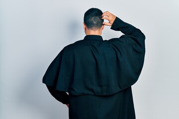 Obraz premium Handsome hispanic man with beard wearing catholic priest robe backwards thinking about doubt with hand on head