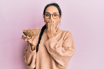 Young hispanic girl holding lentils bowl covering mouth with hand, shocked and afraid for mistake....