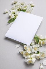 Obraz na płótnie Canvas Composition Of Green Leaves And flowers of jasmine With A Blank Sheet For Text On A gray Paper Background. Natural Layout For Postcard. Flat Lay