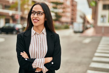 Young hispanic businesswoman smiling happy with arms crossed at the city.