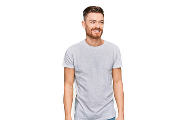 Fototapeta premium Young redhead man wearing casual grey t shirt looking away to side with smile on face, natural expression. laughing confident.