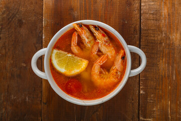 Tom yam soup with shrimps and coconut milk on a wooden table.