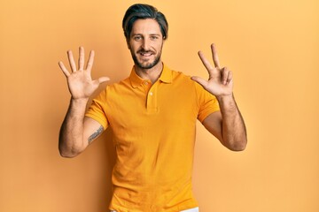 Young hispanic man wearing casual yellow t shirt showing and pointing up with fingers number eight while smiling confident and happy.