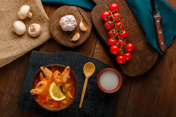 Tom yam soup with shrimps and coconut milk on a table on a black board and a spoon.