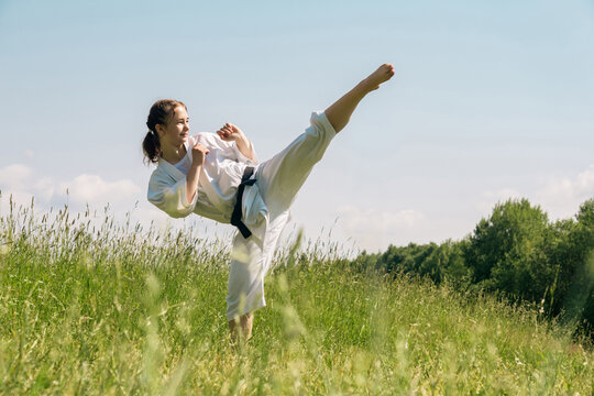 teen girl training karate kata outdoors, performs the mawashi geri kick