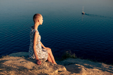 teenager girl in a short haired dress sitting on a cliff over a sea, looking at the ship