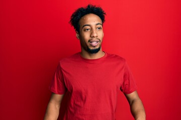 Young african american man with beard wearing casual red t shirt looking away to side with smile on face, natural expression. laughing confident.