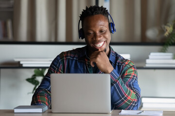 Happy African American man in wireless headphones looking at laptop screen, excited young student...