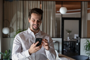Head shot smiling businessman using smartphone standing in office room, positive entrepreneur...