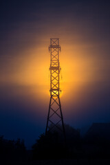 Sun rising through the mist behind a huge high voltage electricity network tower. Summertime scenery of Northern Europe.