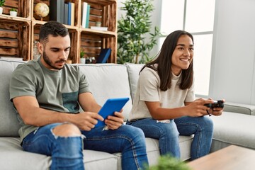 Young latin couple playing video game and using touchpad at home.