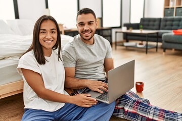 Young latin couple smiling happy using laptop sitting on the floor at bedroom.