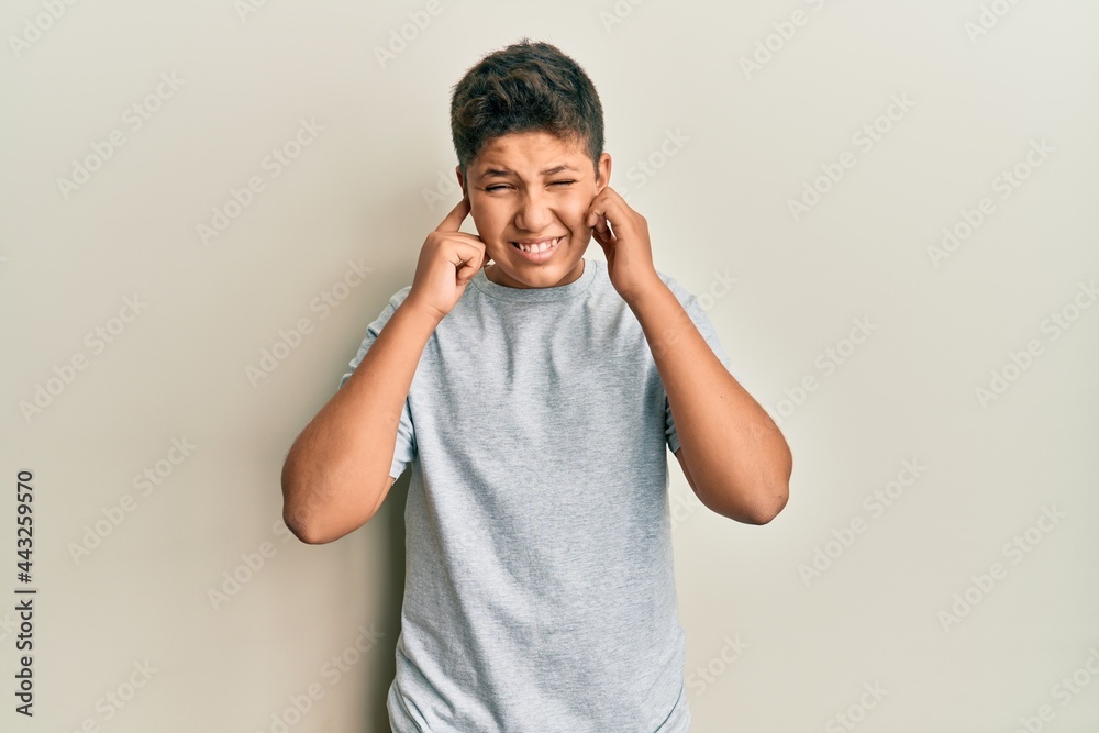 Wall mural Teenager hispanic boy wearing casual grey t shirt covering ears with fingers with annoyed expression for the noise of loud music. deaf concept.