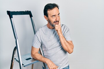 Middle age hispanic man using ladder serious face thinking about question with hand on chin,...