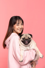 Beauty Asian young woman holding dog pug breed on her arm smile and happiness,Owner hug her cute pet dog with love on pink background,Young girl with adorable dog purebred pug breed looking on camera