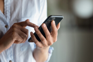 Close up cropped of woman holding smartphone in hand, typing on screen writing message in social...