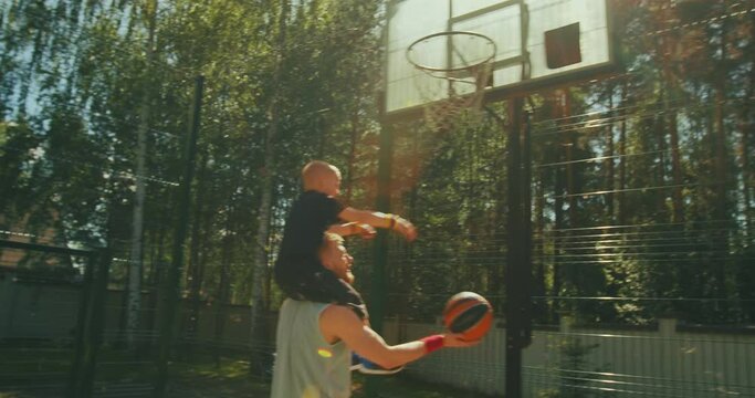Happy family playing basketball, young sports father holding son on shoulders. Kid boy throwing ball in basketball hoop