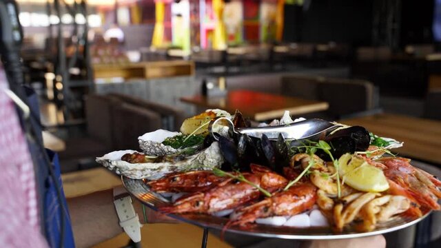 Waiters carries mixed seafood set, lobster shrimp, king prawns, mussels, oysters and squids served on large salver plate for luxury restaurant visitors. Garcon brings traditional meditarian dish.