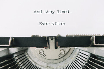 The ending phrase And they lived, ever after (intentionally missing the word happily), typed on a paper sheet in an old vintage typewriter. Closeup shot.
