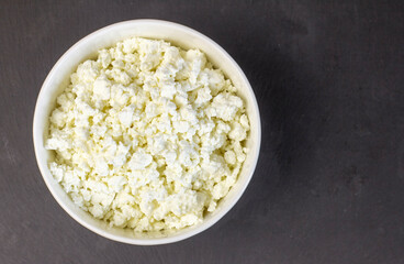 Homemade cottage cheese in a white bowl on a black background.