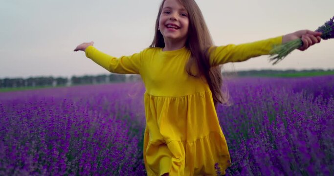 Happy little girl with dress enjoying lavender field with bouquet of flowers