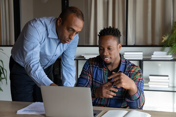African American mentor teaching intern, pointing at laptop screen, executive manager leader...