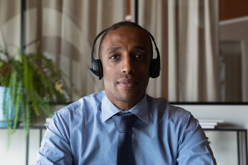 Head shot portrait confident African American businessman in headphones looking at camera, engaged...