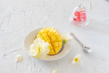 Half a mango cut into wedges and a begonia flower under a glass jar on a painted white table