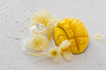 Half a mango cut into wedges and a begonia flower under a glass jar on a painted white table