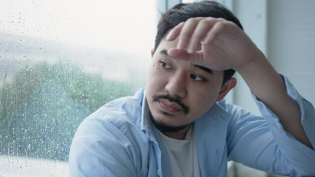 slow motion scene middle eastern man sit alone inside home and look forward through window during thinking about relationship problems with raining mood for mental lifestyle concept