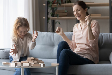 I win. Joyful millennial female foster mother having fun play board game with adopted daughter enjoy funny moment. Happy nanny and laughing preteen girl compete in building tumbling tower at playtime