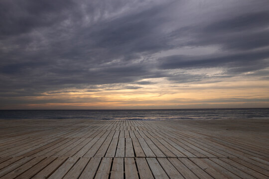 Imagen de una playa con unas tarimas de madera y al fondo un amanecer precioso