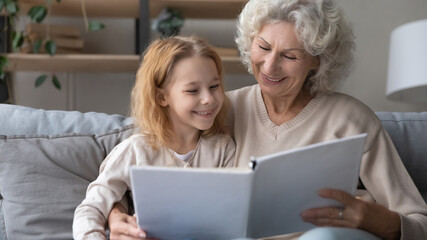 Granny storyteller. Happy smiling small granddaughter and mature grandma enjoy interesting book...