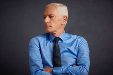 Cropped shot of handsome elderly man wearing shirt and tie while standing with folded arms at dark grey background. Senior man portrait.