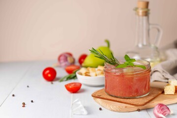 Homemade cold gazpacho puree soup in a glass bowl on a light wooden table with cooking ingredients and croutons. Horizontal, with space
