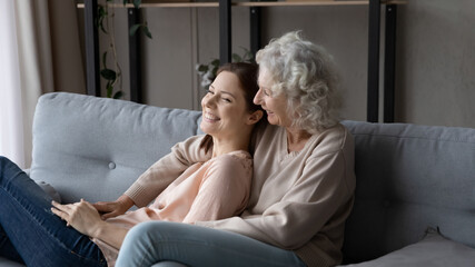 Loving adult daughter resting on comfy couch in warm embraces of beloved supportive retired mommy...