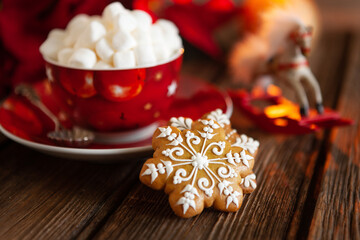 Red cup with hot drink and marshmallow with gingerbread. Christmas concept with poinsettia flower, burning candle and christmas decor. Close-up, selective focus, shallow depth of field.